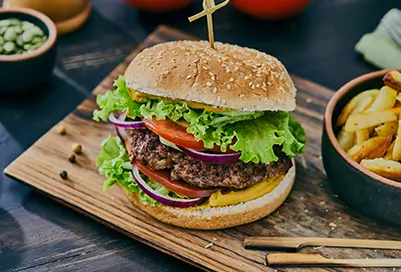 burger with lettuce tomato onion and sesame bun. fries next to it in bowl.